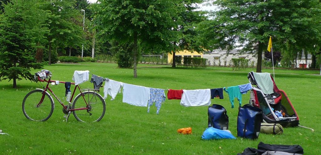 Bike touring washing line strung from bike to Thule chariot trailer with baby gros and baby vests.