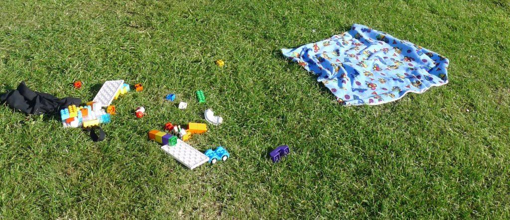 Camping holiday toys: duplo and a fleece blanket on the grass.